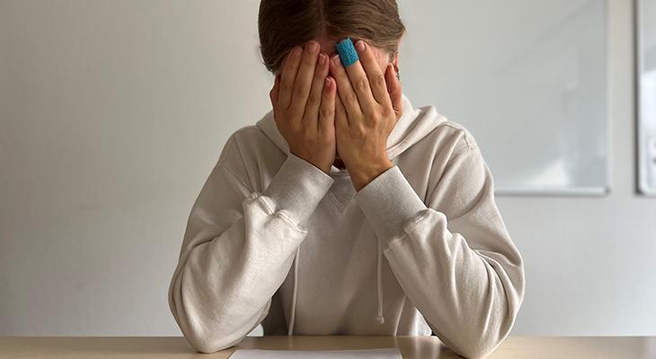 Junger Mensch sitzt am Tisch und verdeckt das Gesicht mit den Händen